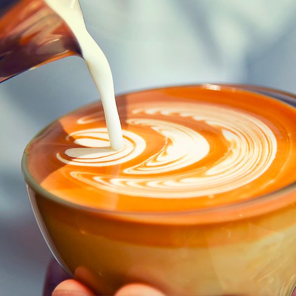 Creamy latte in a mug being topped with beautiful latte art.