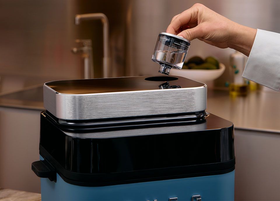 Smeg air fryer with user inserting water tank on top for controlled humidity cooking