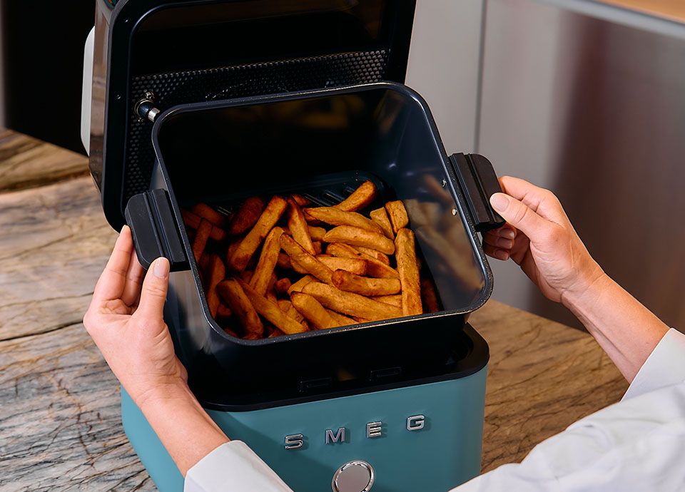 Smeg air fryer with open basket filled with crispy fries on a kitchen countertop