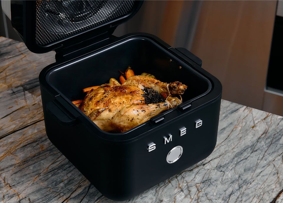 Smeg blue air fryer on a wooden countertop with roasted chicken and potatoes in a modern kitchen setting