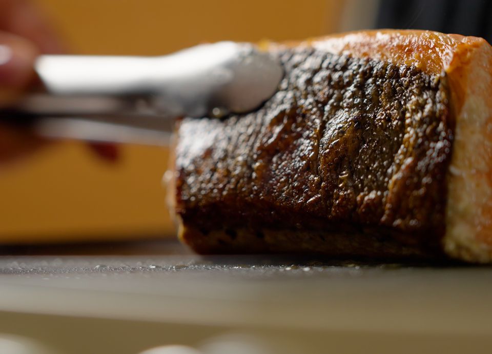 Salmon skin on the surface of the multigrill, seared to perfection with tongs