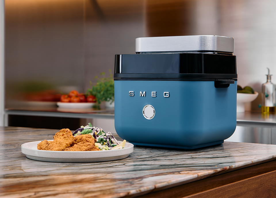 Black SMEG air fryer on a kitchen countertop with crispy fried food and fresh ingredients