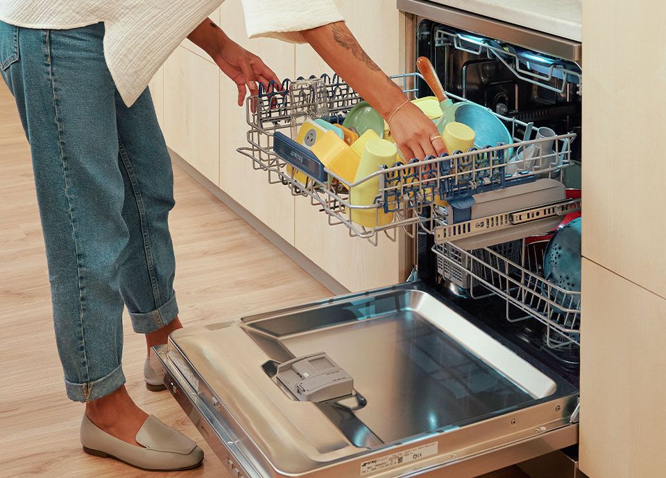 Woman packing a dishwasher with colourful cups and plates