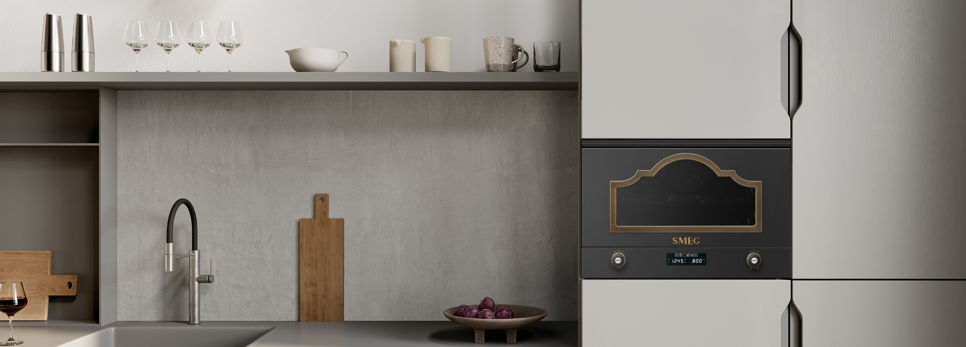 Four micro-ondes encastrable noir et or, style Smeg Cortina, intégré dans une cuisine beige. À gauche, le plan de travail comprend un évier, des ustensiles de cuisine et un plateau de fruits, dans un intérieur moderne et élégant.