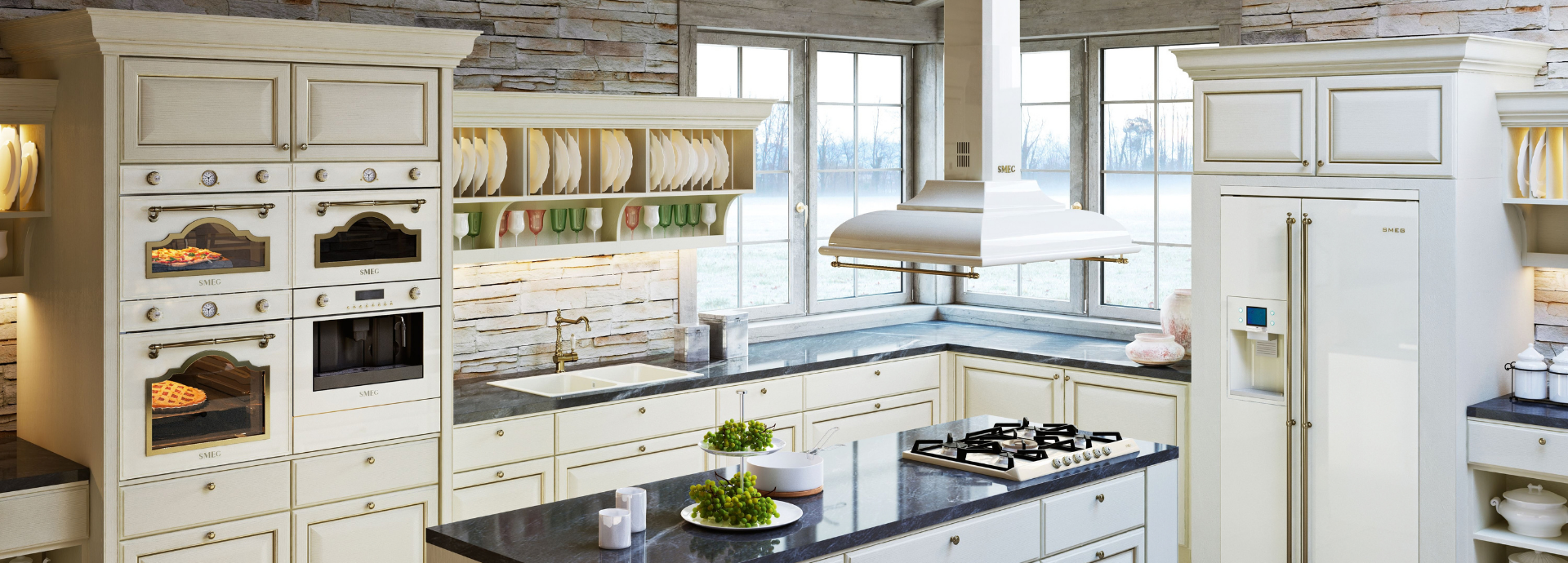 Hotte décorative murale Smeg esthétique Cortina avec finition crème, détails coloris laiton antique et barre porte-ustensiles assortie, suspendue au-dessus d’un îlot central équipé d’une table de cuisson à gaz Smeg crème avec grilles noires et manettes coloris laiton antique. À droite, un réfrigérateur Smeg coordonné avec distributeur d’eau intégré complète l’aménagement. À gauche, une colonne d’appareils encastrables Smeg de la collection Cortina regroupe trois fours et un micro-ondes intégrée aux finitions crème et laiton antique. L’ensemble est mis en scène dans une cuisine classique élégante avec façades moulurées, plan de travail foncé, crédence en pierre naturelle et larges fenêtres apportant une lumière naturelle.