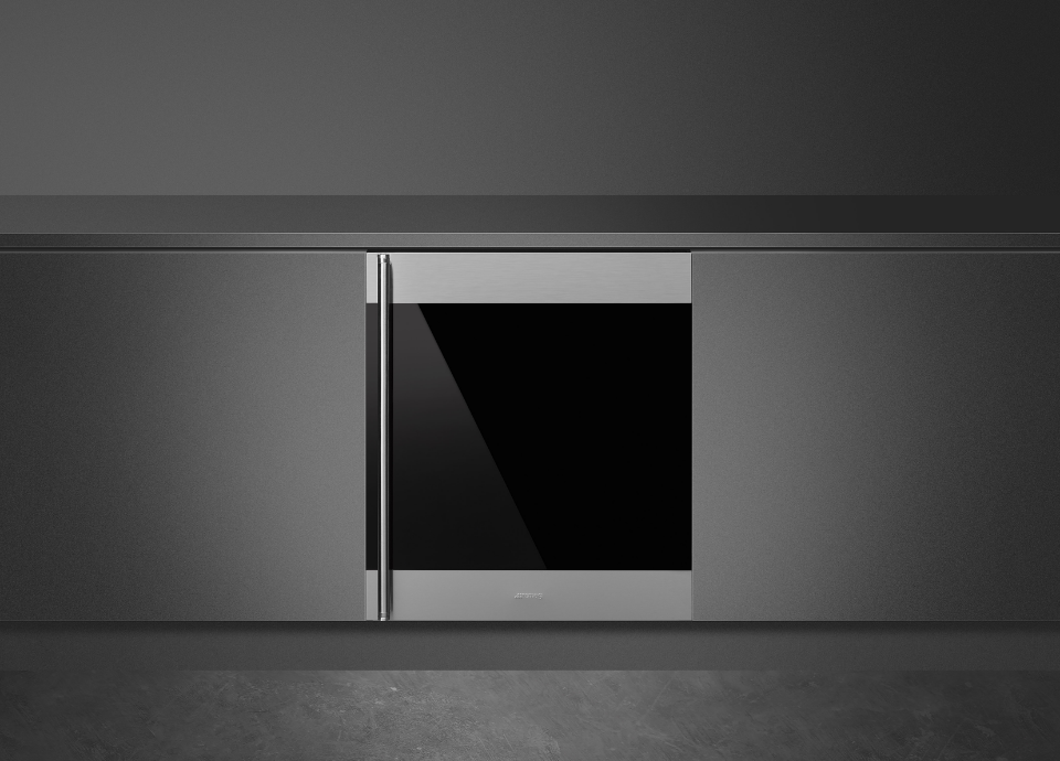 Cave à vin Smeg Classica en inox et noir avec poignée arrondie intégrée sur toute la hauteur du côté gauche de la porte. La cave est encastrée dans un meuble gris et présentée devant un fond noir.