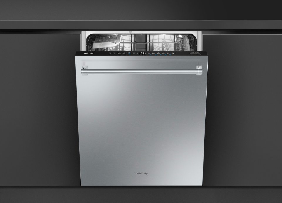 Lave-vaisselle Smeg esthétique Classica avec finition inox anti-traces, intégré sous un plan de travail. Doté d’une façade et d’une poignée horizontale en couleur inox. Avec son bandeau de commande apparent avec affichage numérique, l’appareil constitue l’élément principal de la composition. La porte est entrouverte, laissant apparaître l’intérieur en acier inoxydable avec ses paniers de chargement. L’ensemble est encadré par des meubles de cuisine aux façades foncées