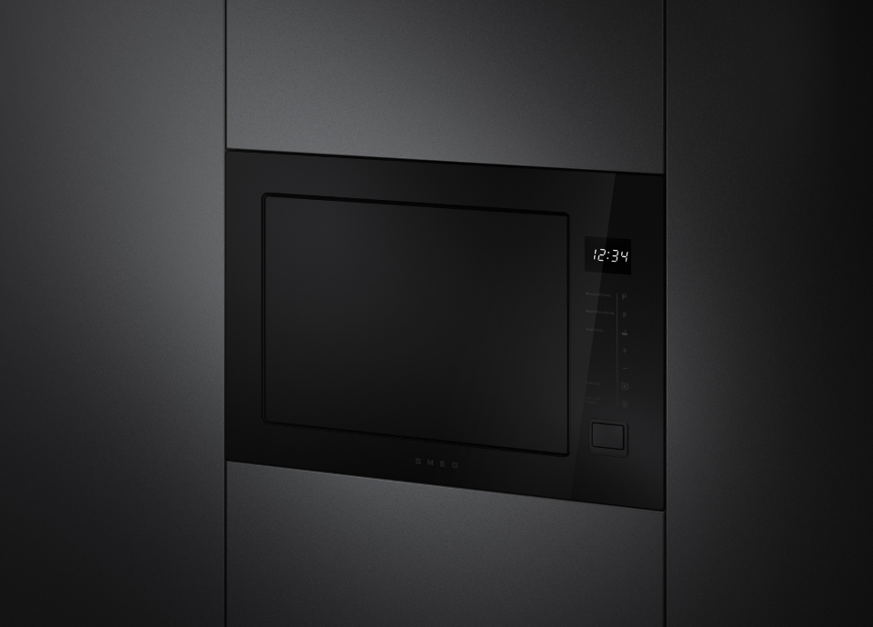 Micro-ondes encastrable Smeg esthétique Musa avec finition noire et verre Noir Eclipse, intégré dans une colonne de cuisine contemporaine aux façades gris foncé. Doté d’une façade en verre noir, d’un affichage numérique discret et de commandes tactiles latérales, il se distingue par son design minimaliste aux lignes épurées caractéristique de la collection Musa.