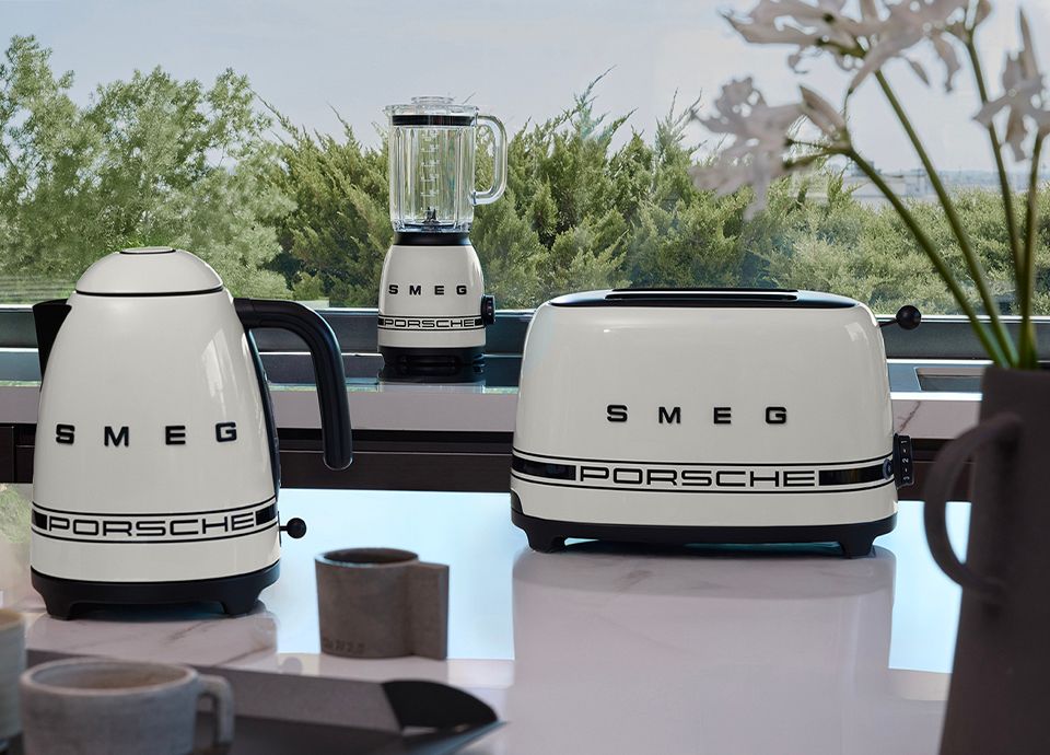Ensemble de petit électroménager Porsche x SMEG de la collection Carrara White. Bouilloire, blender et grille-pain posés sur une table dans une cuisine.