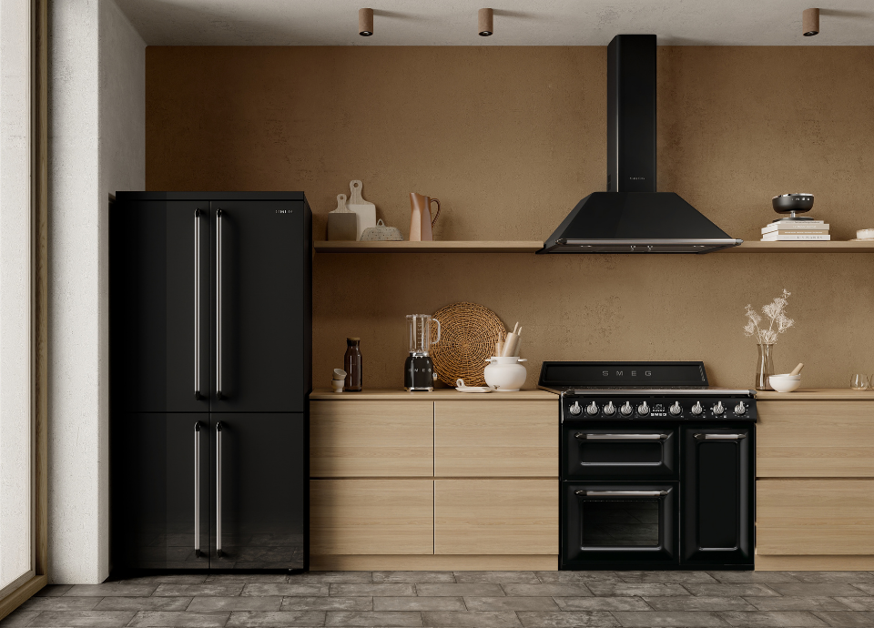 Réfrigérateur multi-portes Smeg esthétique Victoria noir avec poignées verticales en couleur inox, associé à un piano de cuisson Smeg noir et à une hotte décorative murale noire dans une cuisine contemporaine en bois clair. L’ensemble est mis en valeur par des étagères, des accessoires de cuisine et des petits appareils électroménagers Smeg dans une ambiance chaleureuse et moderne.