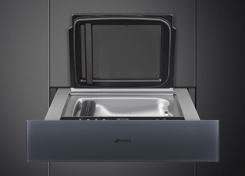 Tiroir sous vide Smeg noir encastré dans un meuble noir, présenté ouvert avec un intérieur en inox. À l’intérieur, des boutons de réglage permettent de contrôler les différentes fonctions de mise sous vide. Le compartiment dispose également d’un couvercle intérieur qui s’ouvre vers le haut pour faciliter l’utilisation.
