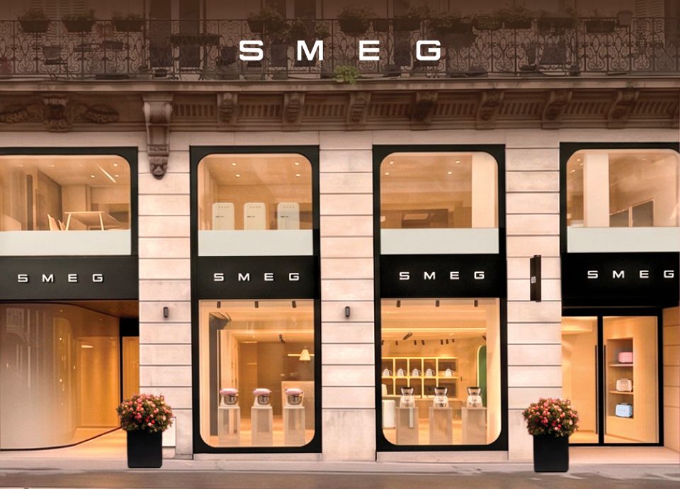 Flagship Store SMEG Paris, façade de la boutique aux grandes vitrines arrondies mettant en scène une sélection d’appareils emblématiques de la marque. L’espace, baigné d’une lumière chaleureuse, expose des réfrigérateurs design Années 50 et du petit électroménager SMEG, reflétant l’univers premium et le savoir-faire italien de la marque.