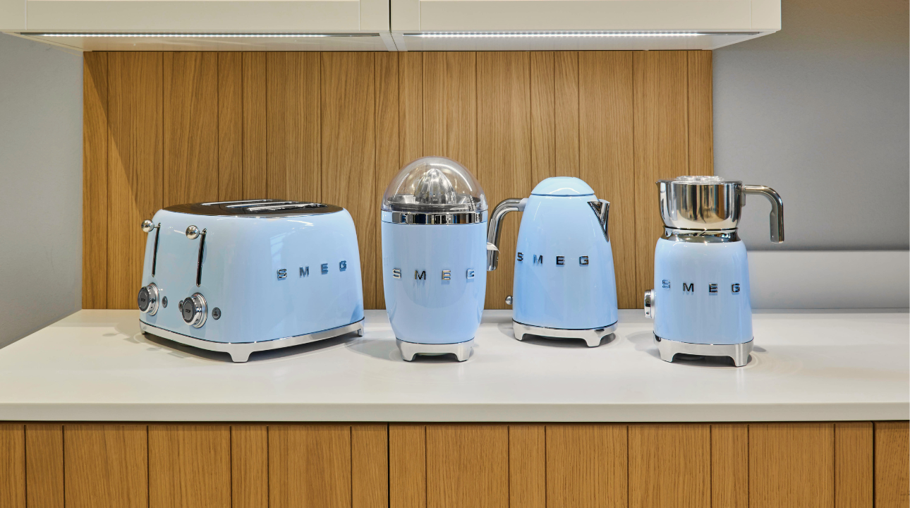 Ensemble petit-déjeuner bleu azur SMEG bouilloire bleue, grille-pain, presse-agrumes et mousseur à lait sur un plan de travail.