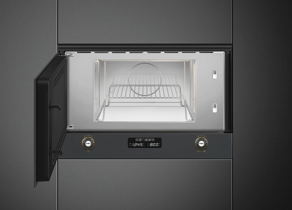 Micro-ondes grill encastrable Smeg avec façade noire, deux boutons de commande dorés sous la cavité et écran tactile central, présenté ouvert avec vue sur sa cavité intérieure blanche, sur fond noir avec un éclairage mettant en valeur son design moderne .