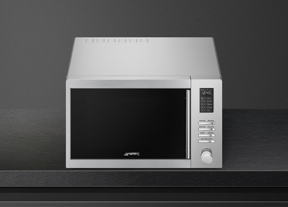 Four micro-ondes pose libre Smeg avec façade noire, contour inox, présenté sur fond noir avec un éclairage mettant en valeur son design moderne.