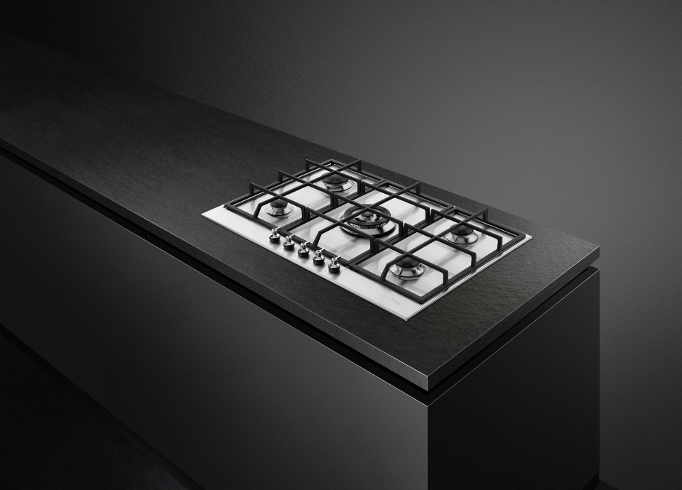 Plaque de cuisson gaz Smeg en inox avec grille noire, intégrée sur un plan de travail mat. Le fond de l'image est noir, créant un contraste élégant entre l’inox, les grilles noires et les surfaces sombres.
