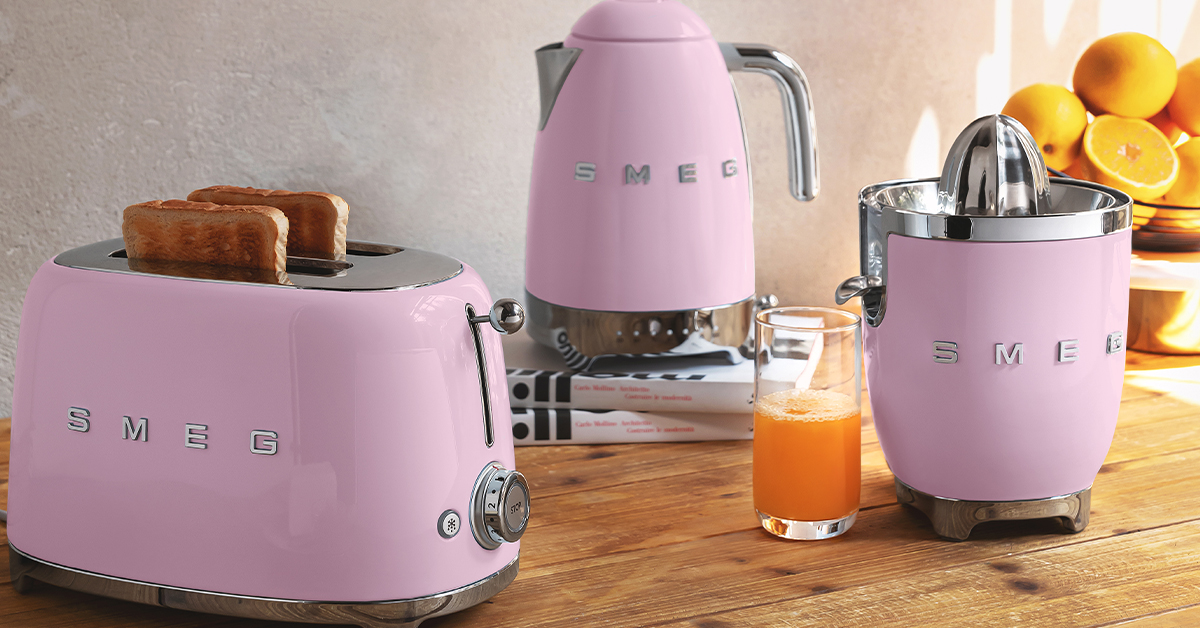 Ensemble de petit déjeuner Smeg rose. Grille-pain rose, bouilloire rose et presse-agrumes rose sur un plan de travail en bois.