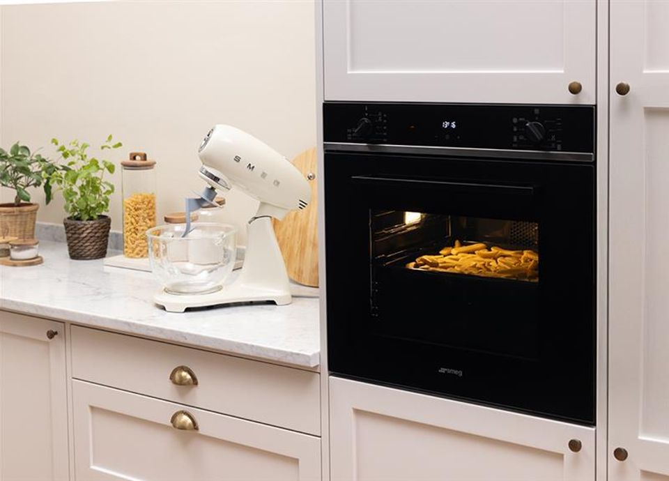 Forno da incasso Smeg con vetro nero ambientato in una cucina moderna con impastatrice bianca sul topo di lavoro