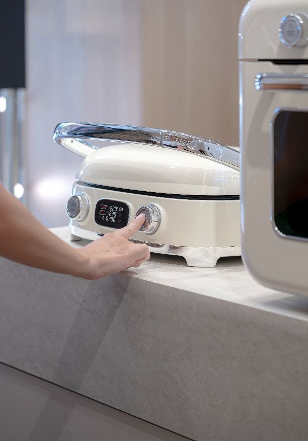 Persona che interagisce una griglia elettrica multifunzione SMEG nell'area espositiva dei piccoli elettrodomestici dello SMEG Store Bologna.