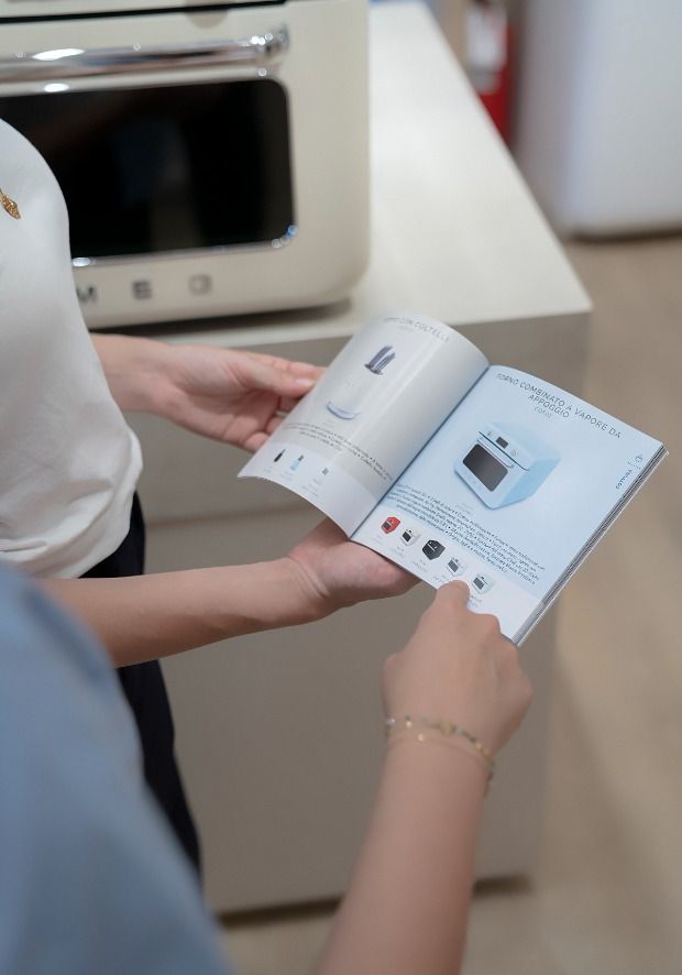 Presso lo SMEG Store Bologna, una persona consulta insieme a un addetto un catalogo di elettrodomestici SMEG, ricevendo informazioni e consigli personalizzati per orientare la scelta del prodotto più adatto