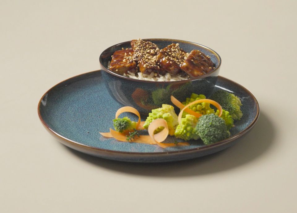 Tofu teriyaki servido con semillas de sésamo y verduras en un plato de cerámica azul claro