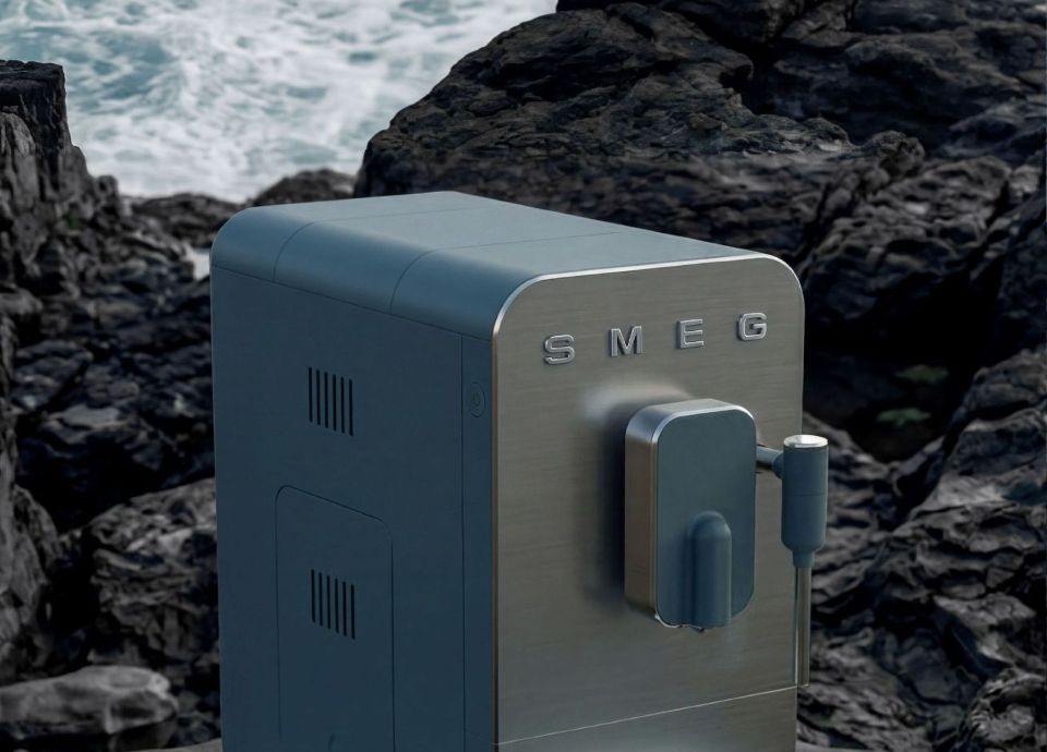Air fryer SMEG w odcieniu Storm Blue, o kompaktowej, kwadratowej formie z ciemnym frontem ze szkła i metaliczną górną częścią, ustawiona na skalistym nadmorskim podłożu z morzem w tle.