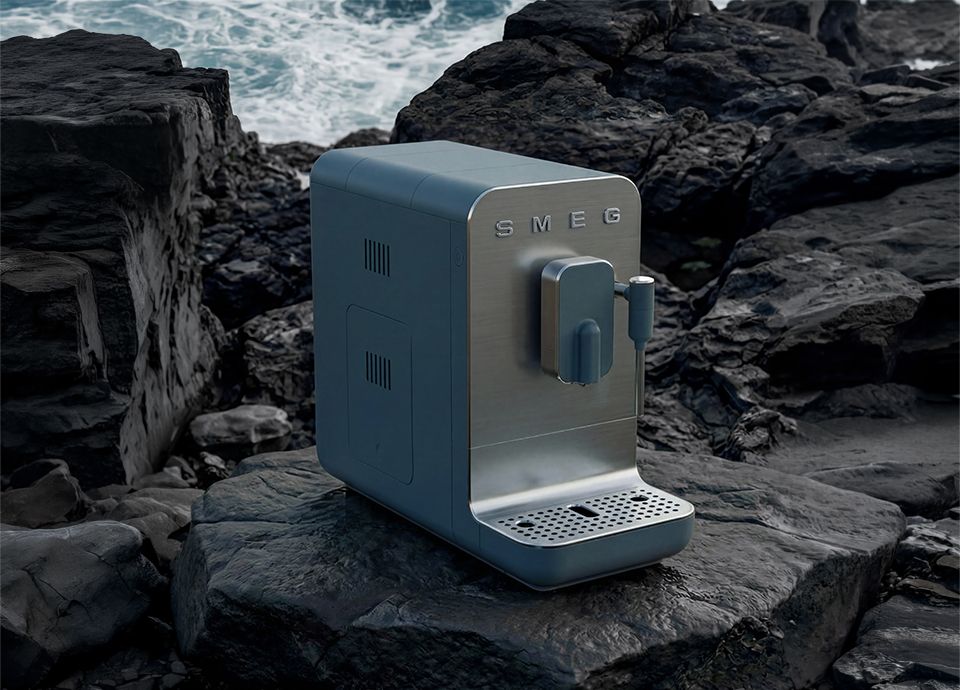Storm blue SMEG bean to cup coffee machine, showcased among dark coastal rocks overlooking the sea.