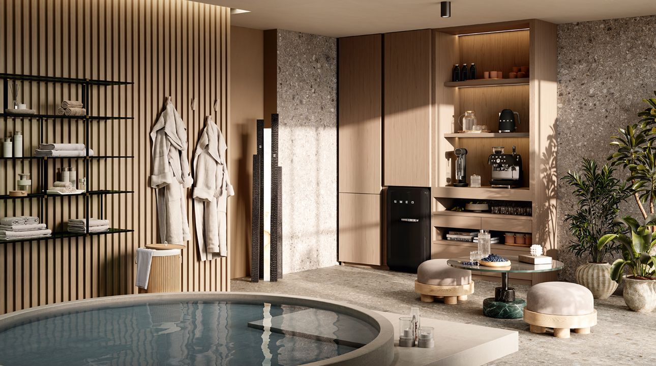 Spacious modern kitchen with SMEG appliances in matte storm blue finish, including a retro-style refrigerator, range cooker, and extractor hood, set within dark cabinetry, a light wooden dining table, and large windows opening onto a garden.