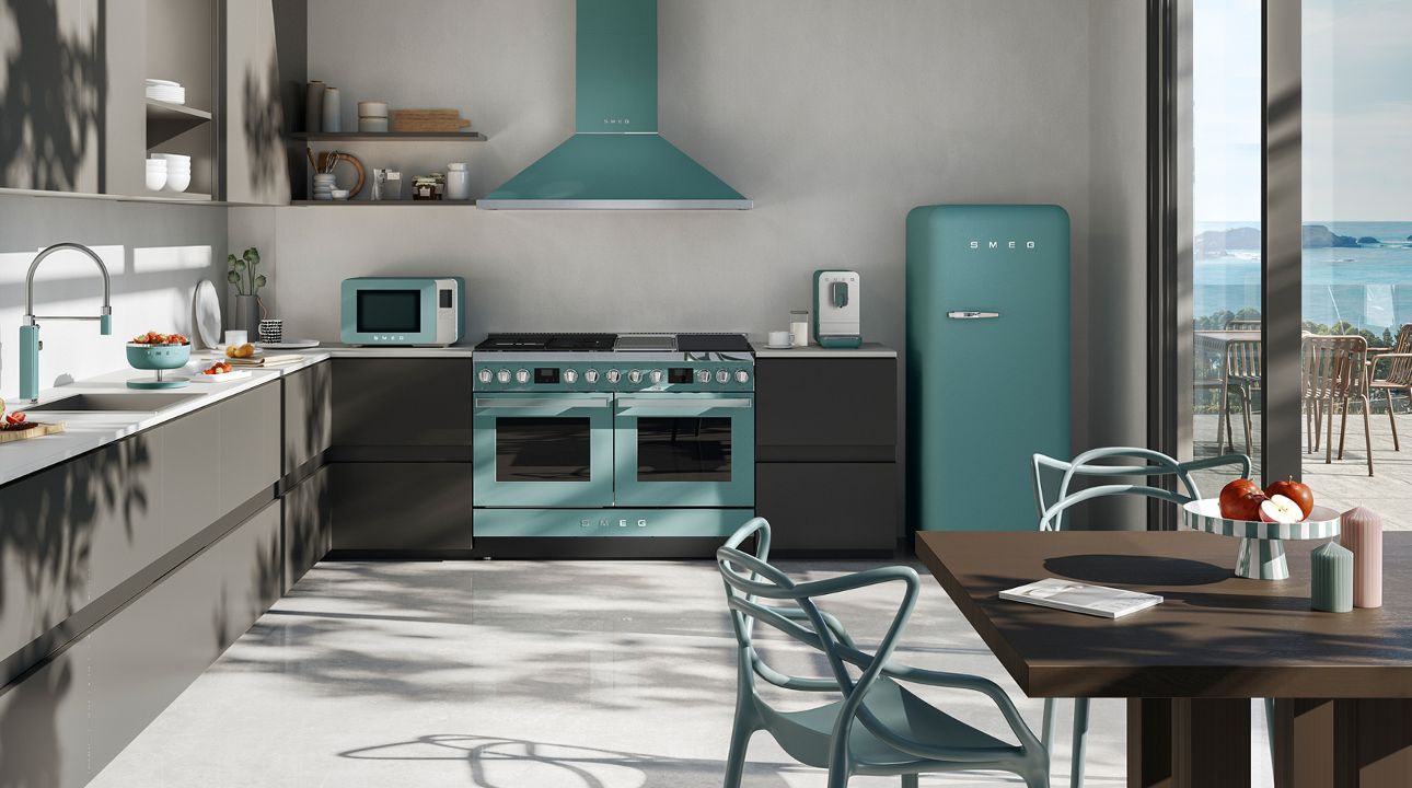 Bright multifunctional living space featuring SMEG appliances in emerald green finish, including a retro-style refrigerator and small countertop appliances on a wooden sideboard, set alongside a fitness area with gym equipment, light wood flooring, and large windows with sheer curtains.