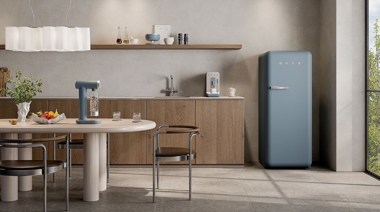 Compact kitchen corner featuring SMEG appliances in emerald green finish, including a retro-style refrigerator, soda maker, and small countertop appliances, set against warm wood cabinetry and burgundy lower units with a dining area to the side.