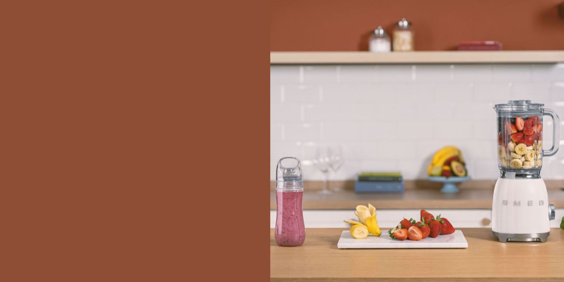 Batidora de vaso blanca junto botella rellena de batido y frutas al rededor, sobre encimera de madera