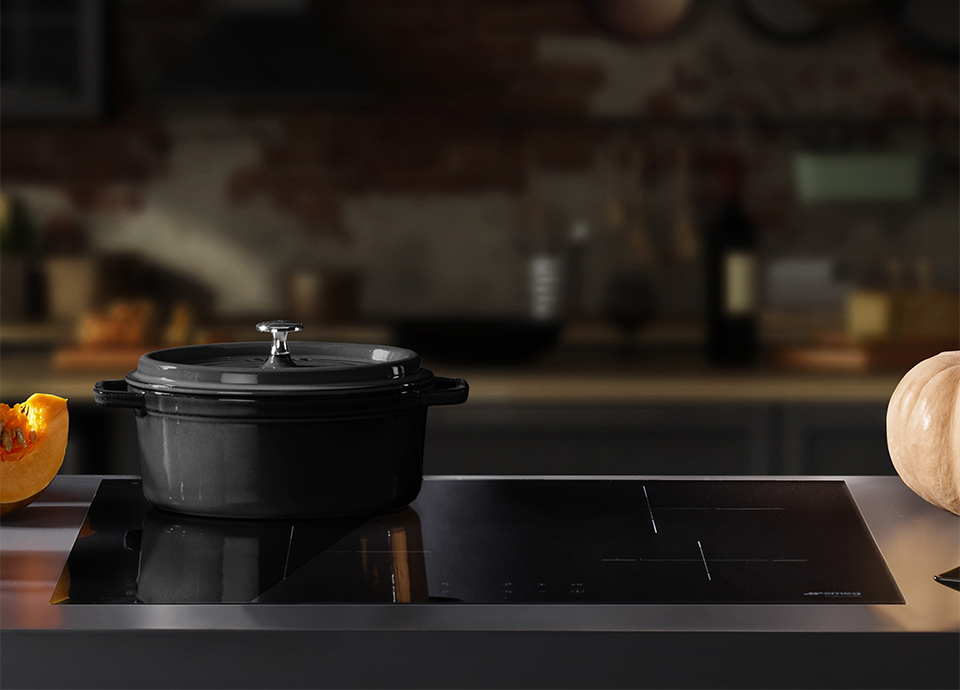 A black induction hob inlaid in a stainless steel surround. Also shows a sliced pumpkin and grey cooking pot