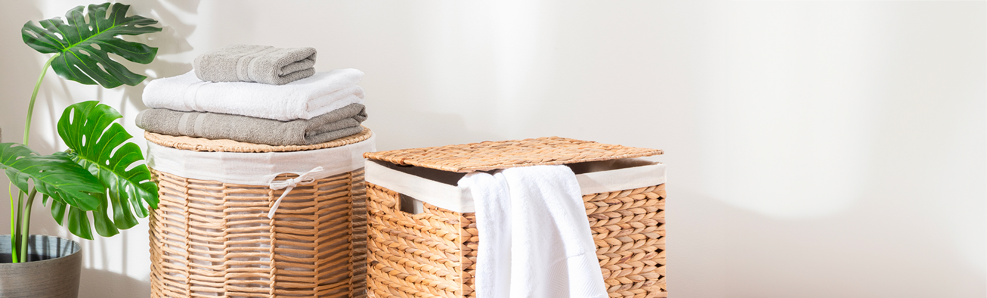 Laundry towels on a wicker laundry basket with a monstera plant