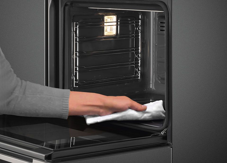 An open oven being cleaned with a white cloth to indicate how much dirt has already been removed by the pyrolytic and vapor cleaning system