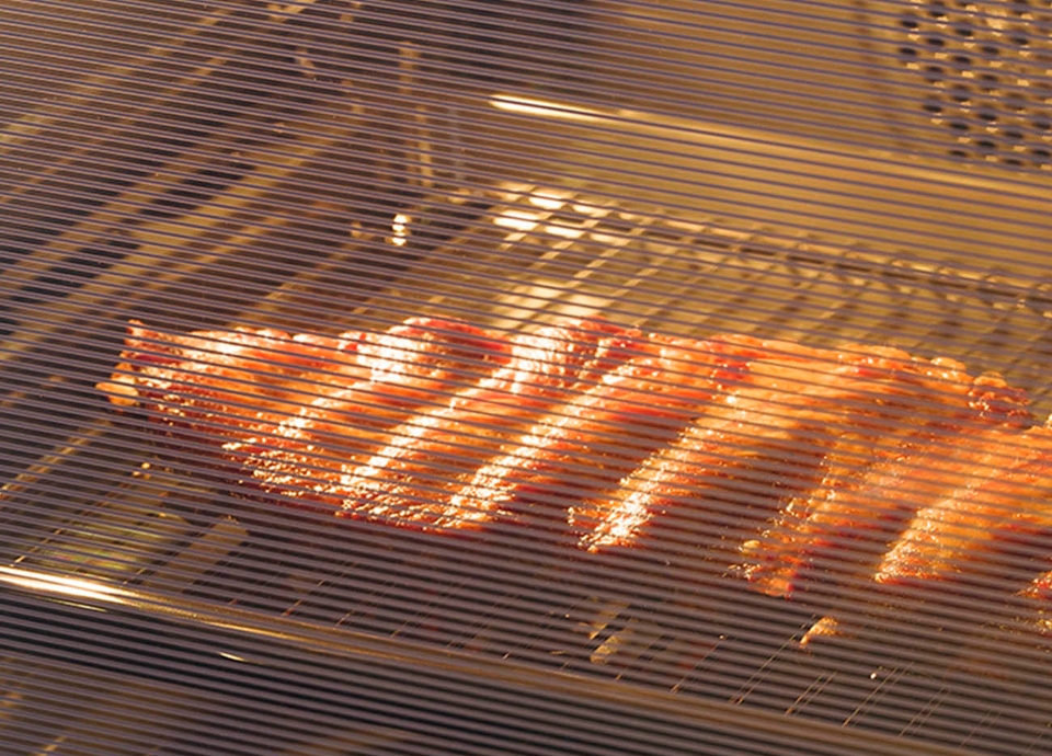 A view through an oven door with the internal light on, with meat grilling inside