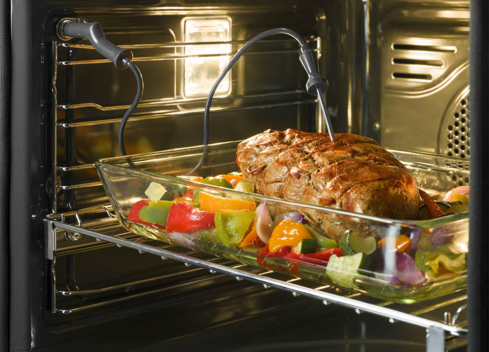 An open oven with a temperature probe piercing a large joint of meat