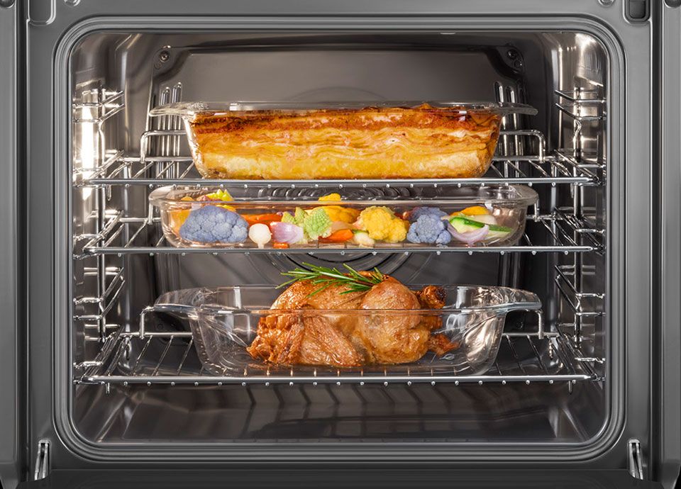 A fan assisted oven with 3 shelves of food cooking including a chicken and vegetables