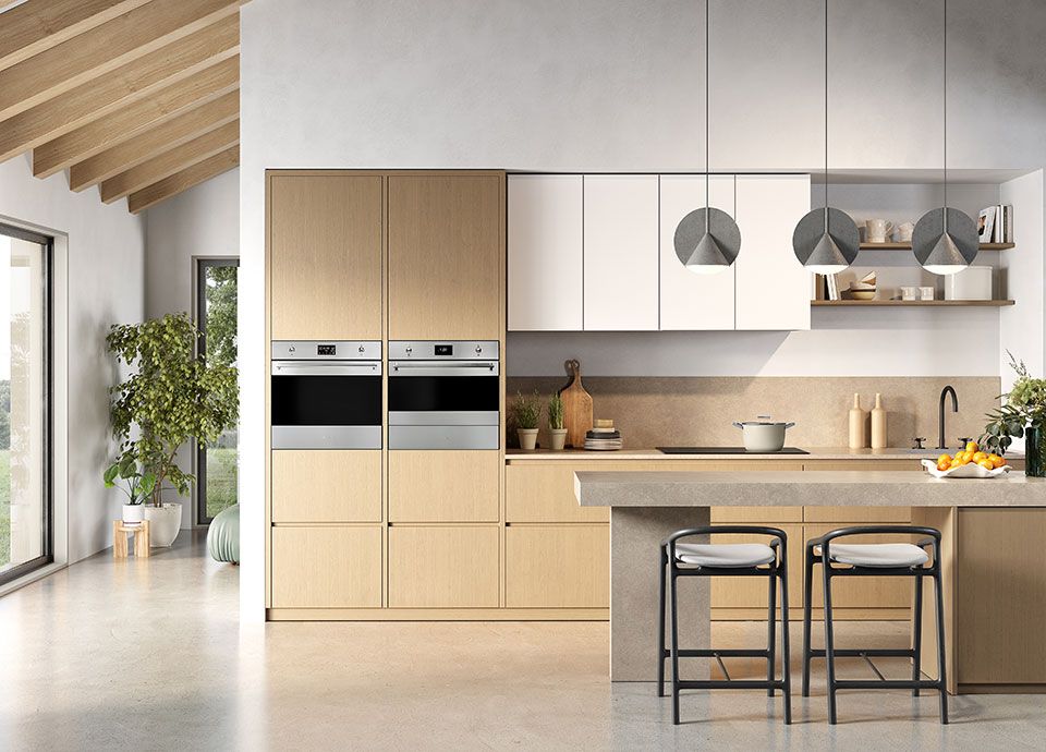 A bright and modern kitched with light wooden units, and two integrated Smeg ovens (stainless steel) positioned side-by-side across two floor-to-ceiling columns of kitchen units