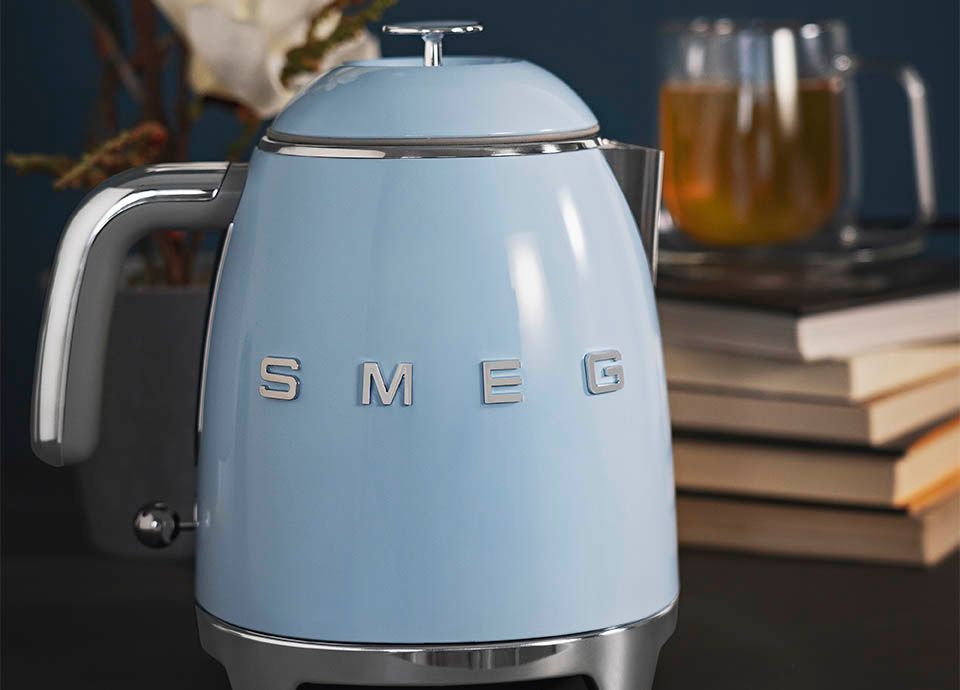 Smeg's mini kettle in light blue with a chrome and grey curved handle, and chrome base.