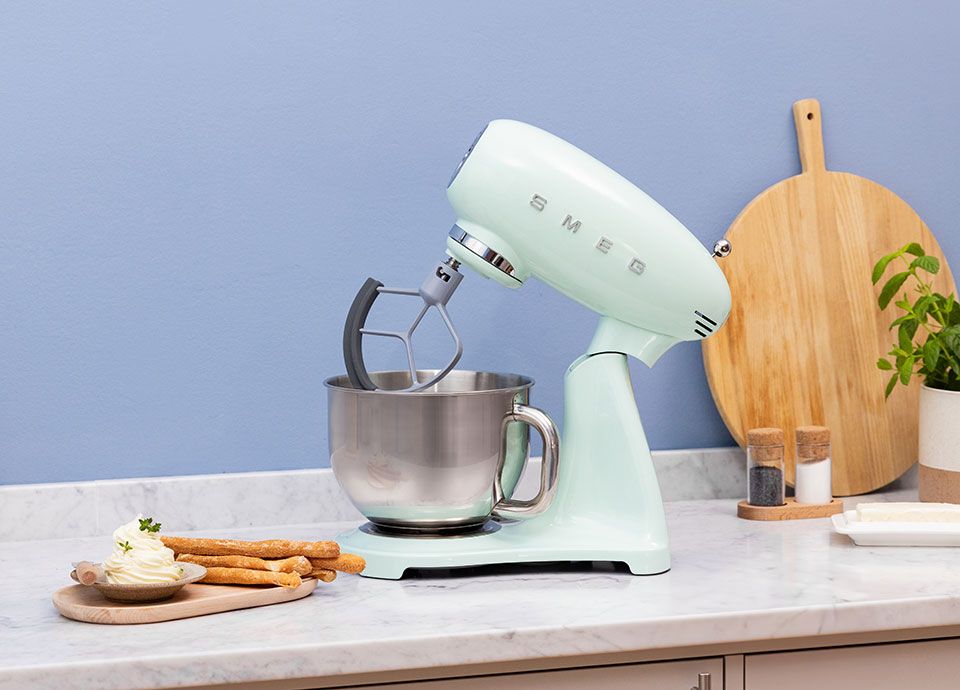 Pastel green SMEG stand mixer with a stainless steel bowl on the kitchen countertop.