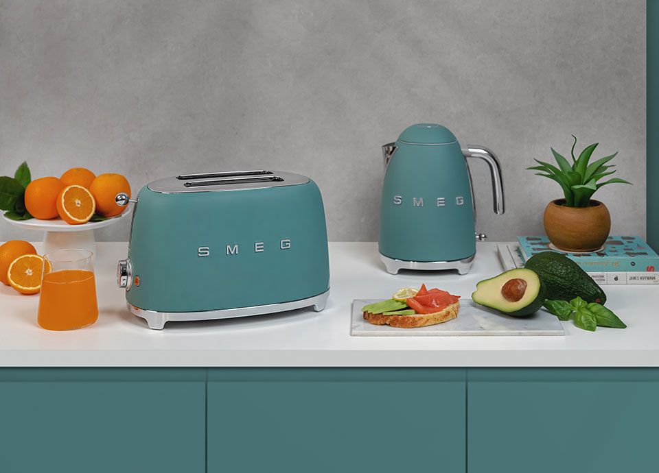 Our emerald green kettle and toaster set, placed on a white worktop, above emerald green kitchen units. To the left are vibrant fresh oranges providing a delightful pop of colour contrast.