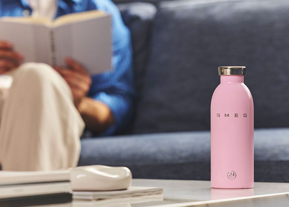 Pink Smeg water bottle on table while man is reading