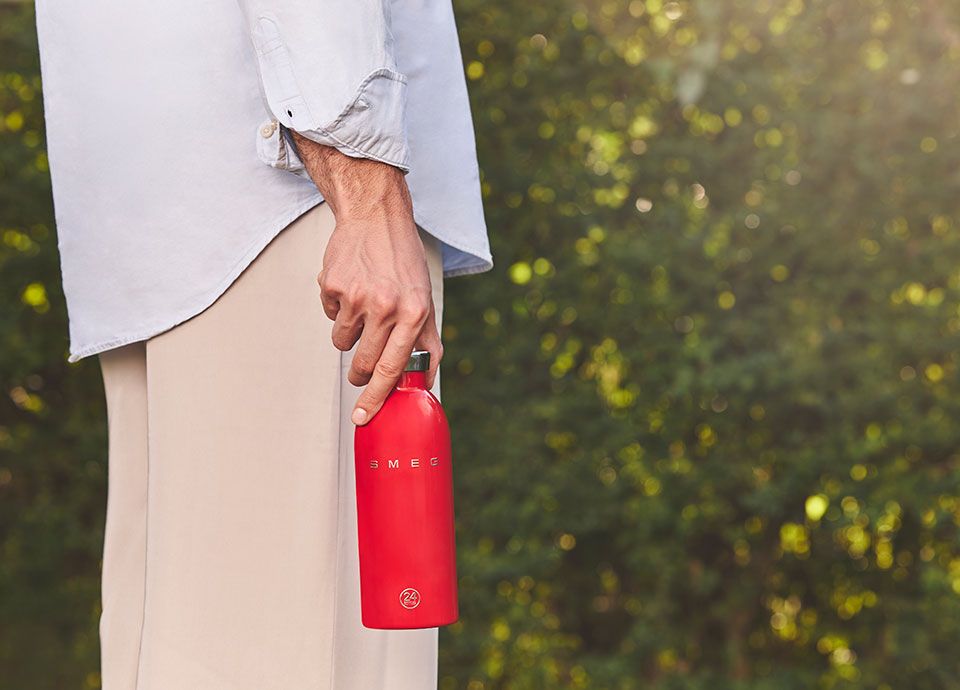 Red Smeg water bottle being held by person outside on a walk