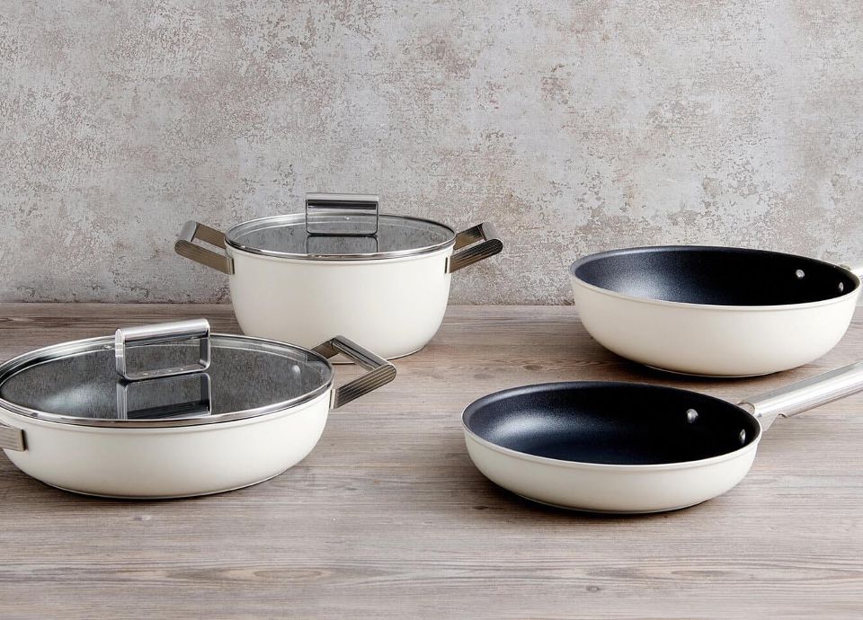 Four cream Smeg cookware pans and dishes on a wooden worktop