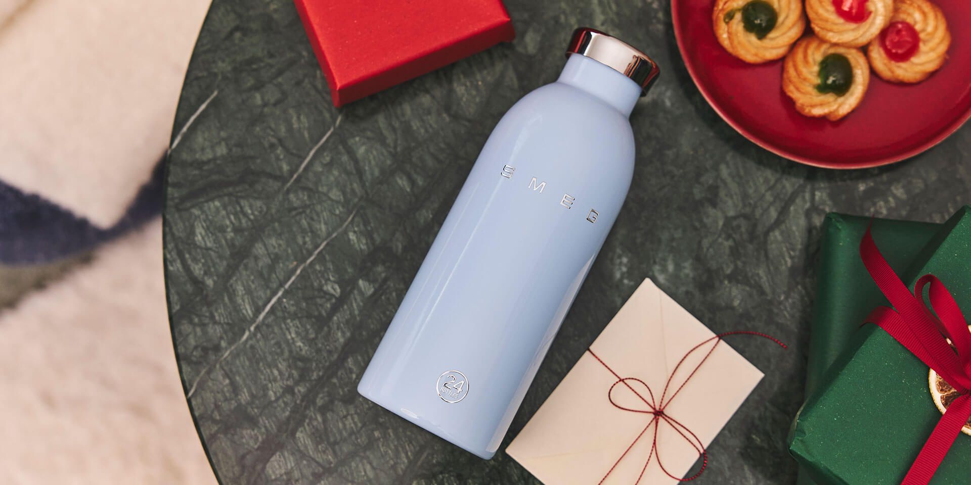 Pastel pink Smeg water bottle on table with person reading in the background on a dark sofa