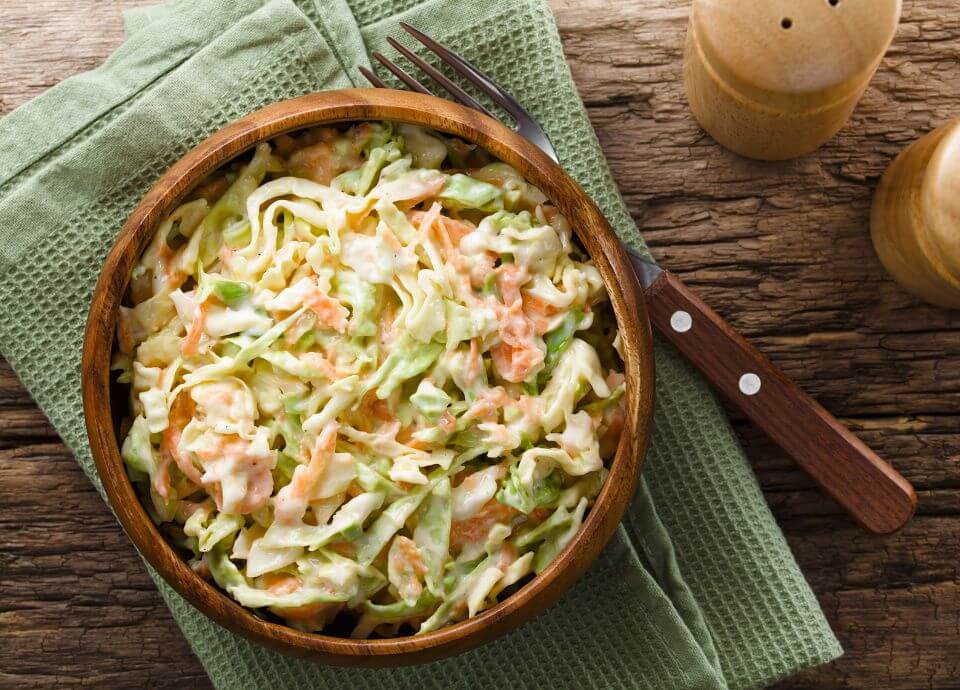 Creamy coleslaw served in a wooden bowl, with shredded cabbage and carrot on a rustic wooden table