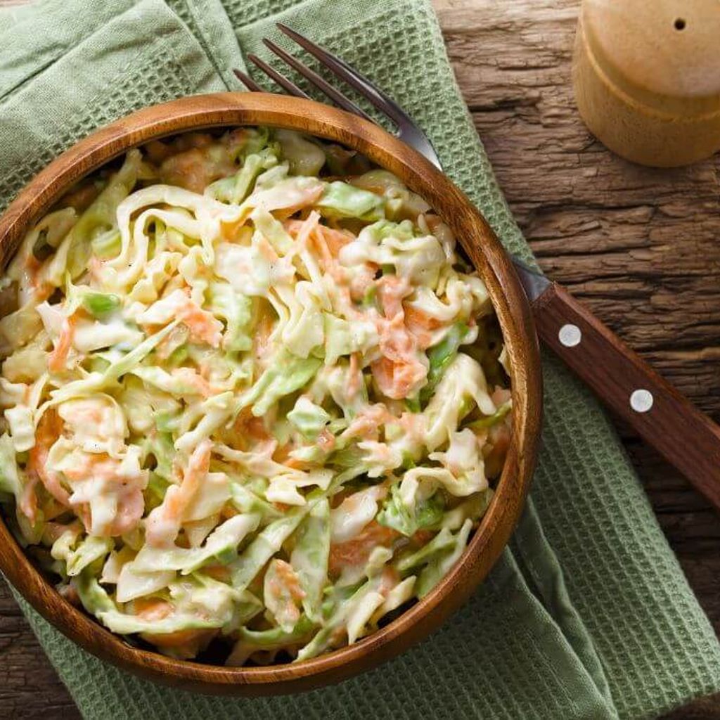 Creamy coleslaw served in a wooden bowl, with shredded cabbage and carrot on a rustic wooden table