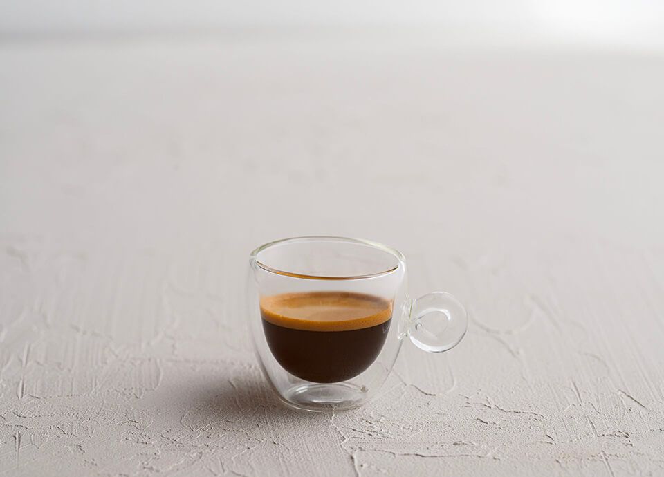 Single shot of espresso served in clear glass, showcasing thick golden crema.