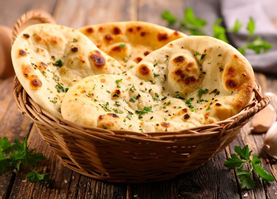 Warm flatbreads sprinkled with herbs, stacked in a woven basket on a rustic wooden table