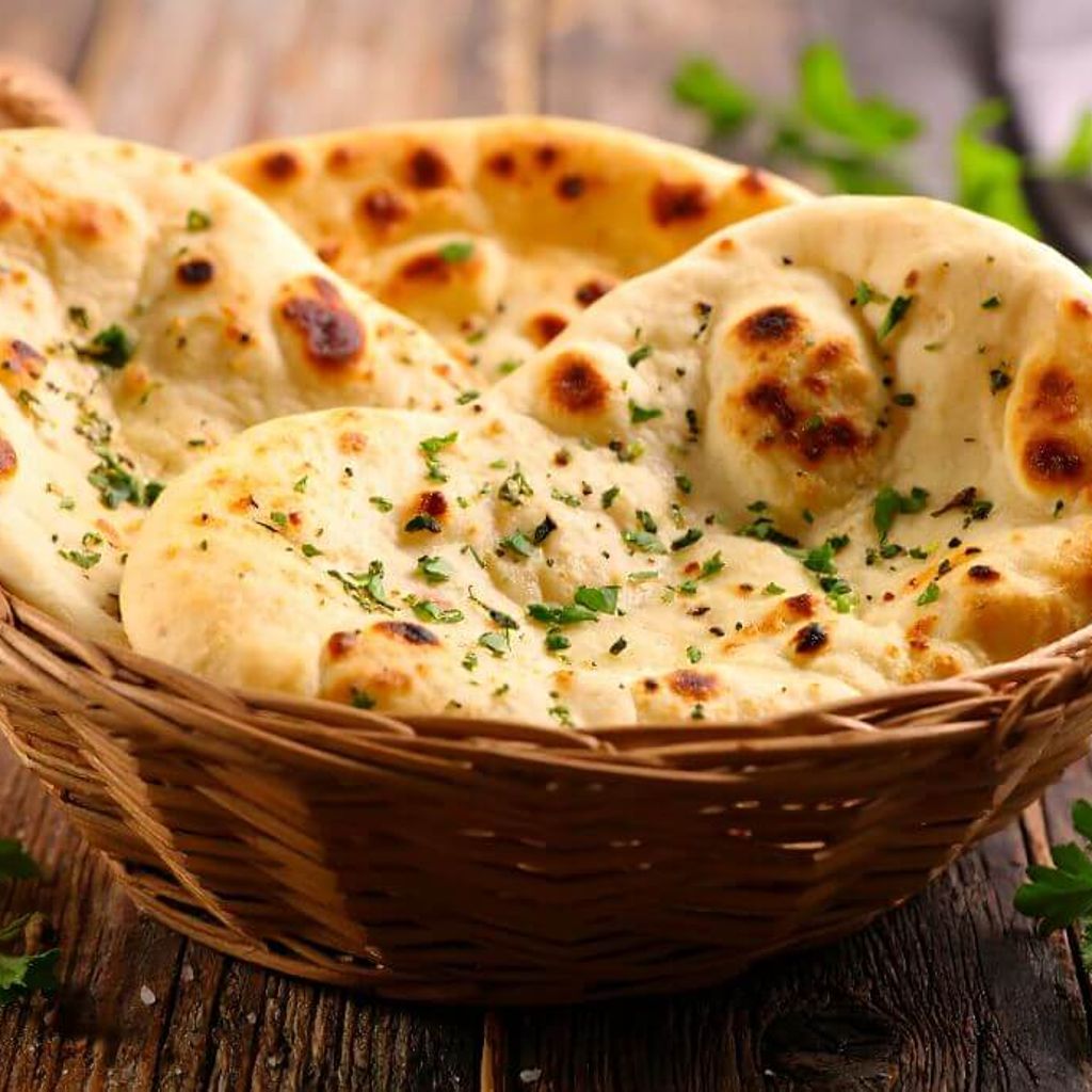 Warm flatbreads sprinkled with herbs, stacked in a woven basket on a rustic wooden table